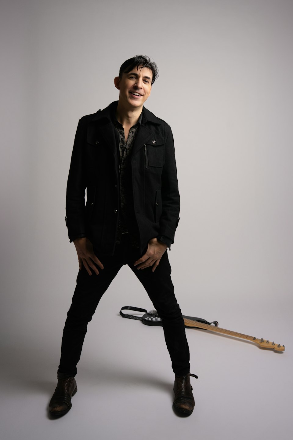 Mann in schwarzer Jacke steht neben einer E-Gitarre.